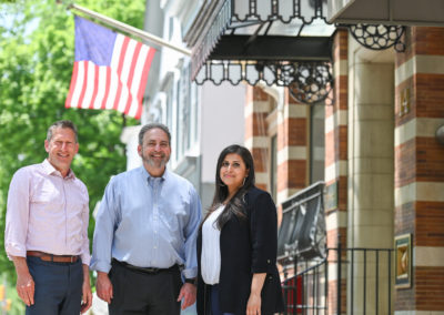 Andrew Zwicker, Roy Freiman, and Sadaf Jaffer pose for a team photo under and American flag.
