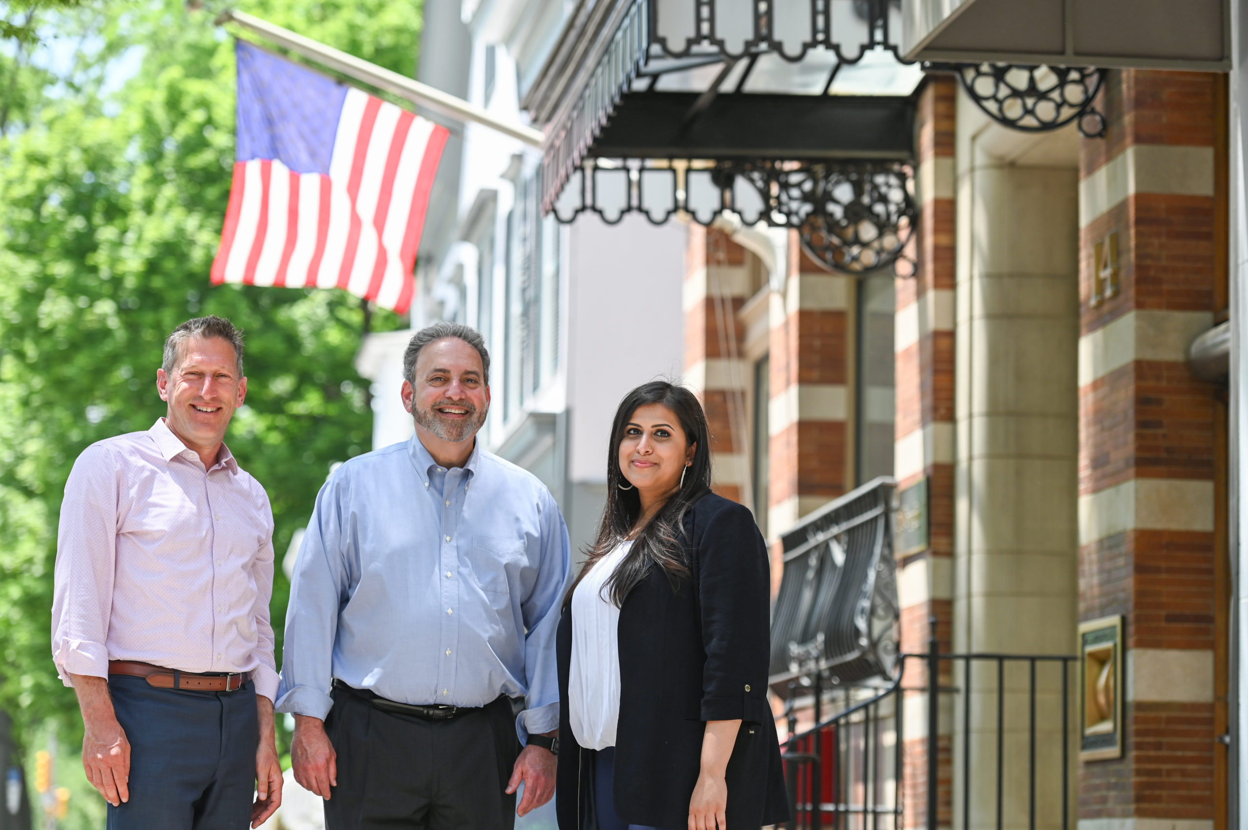 Andrew Zwicker, Roy Freiman, and Sadaf Jaffer pose for a team photo under and American flag.